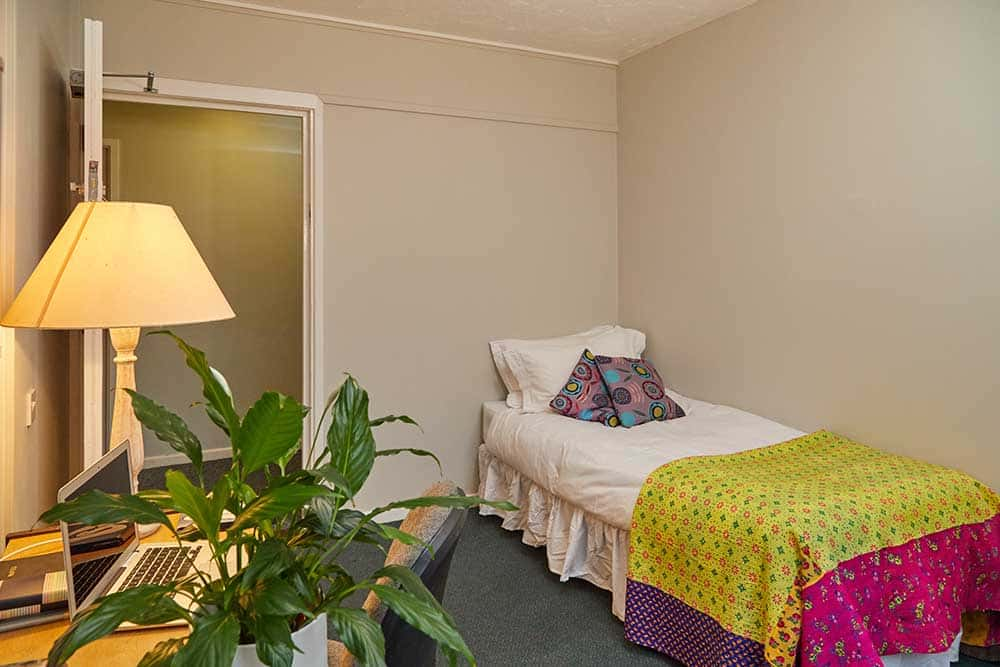 Bedroom at Beechcroft, university halls at Norwich University of the Arts with yellow bedspread, plant and lamp