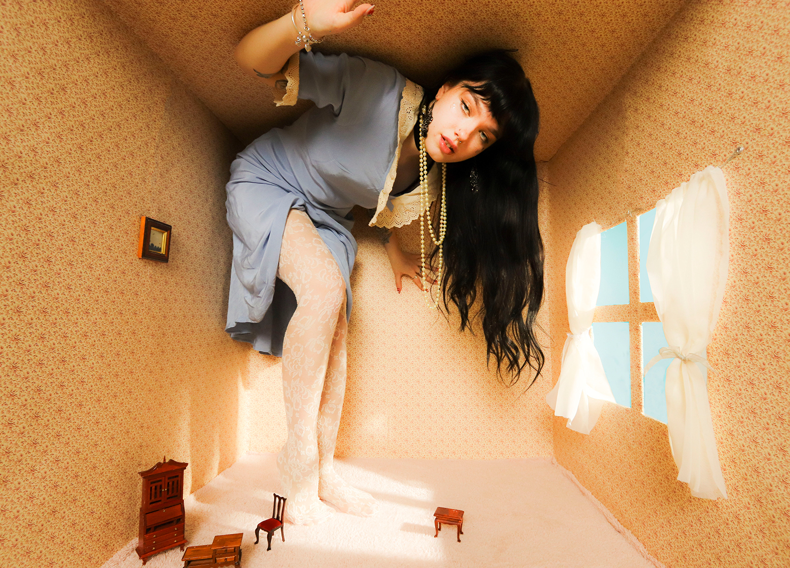 Model crouches to fit under the ceiling in a large dolls house room, making her look like a giant