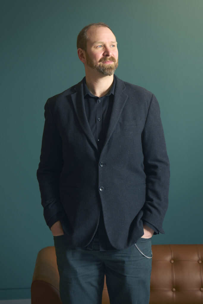 Staff portrait image of Mark Wickham, ‪Director of Computer Arts and Technology at Norwich University of the Arts‬. Mark wears a buttoned up shirt under a suit jacket