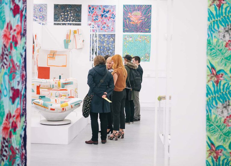 photo of three women looking at handmade armchair which features digitally printed fabric made by a Norwich University of the Arts student