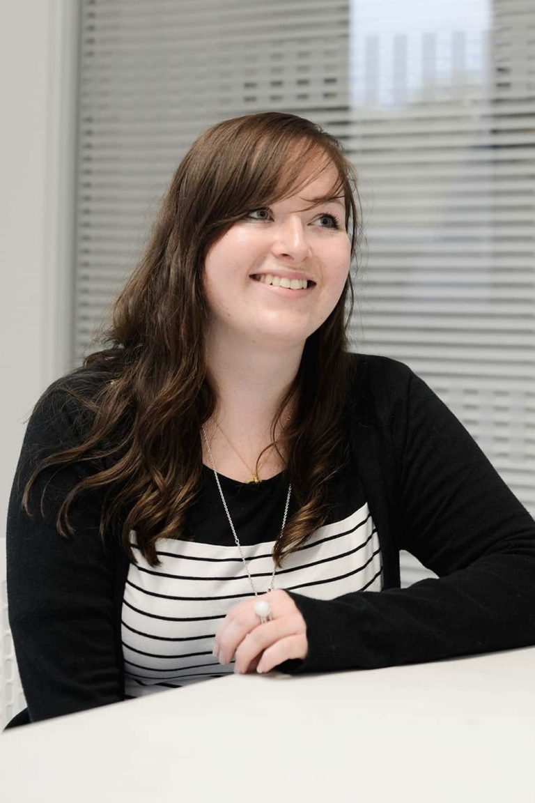 photo of alum Alice Bridle smiling and looking away from camera with long brown hair and an open long sleeved top