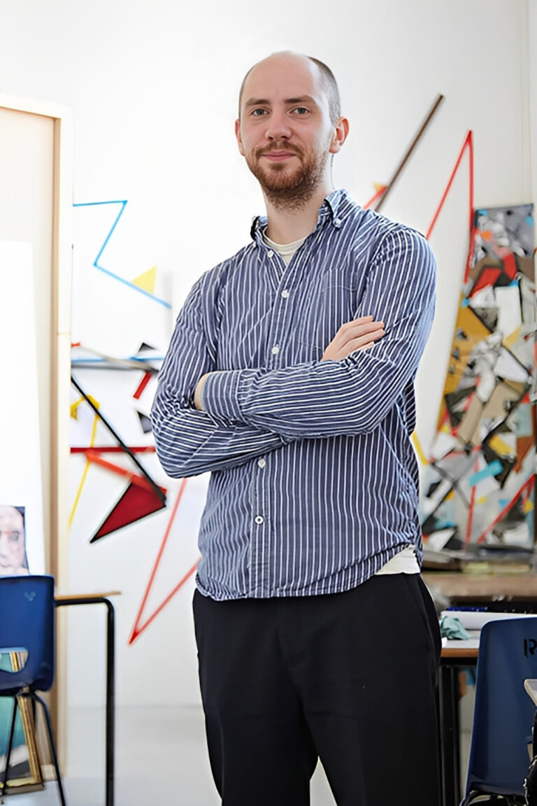 portrait photo of senior lecturer craig barber standing with arms crossed and looking at camera with short brown hair and a long sleeved vertically striped blue and white shirt