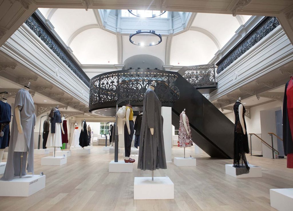 Photo of Norwich University of the Arts building Boardman House atrium with a black metal circular staircase in the centre and many clothing mannequins around the lower level featuring a variety of BA Fashion clothing items