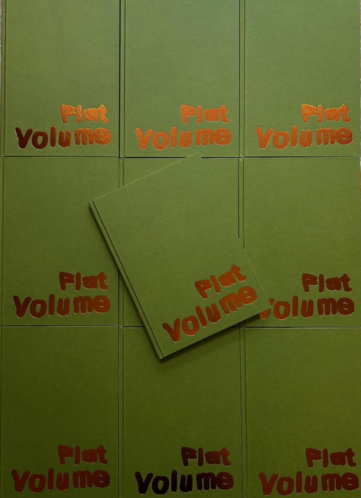 Several green books with "Flat Volume" in shiny orange letters on the covers are arranged in a grid. One book is placed diagonally on top of the others.