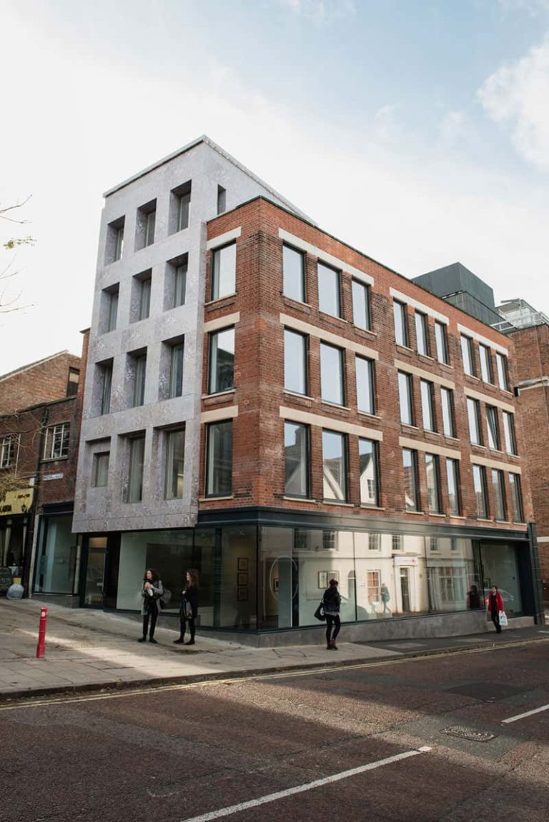 photo of Norwich University of the Arts building Cavendish House exterior shows five story grey concrete with red brick addition and glass lower floor