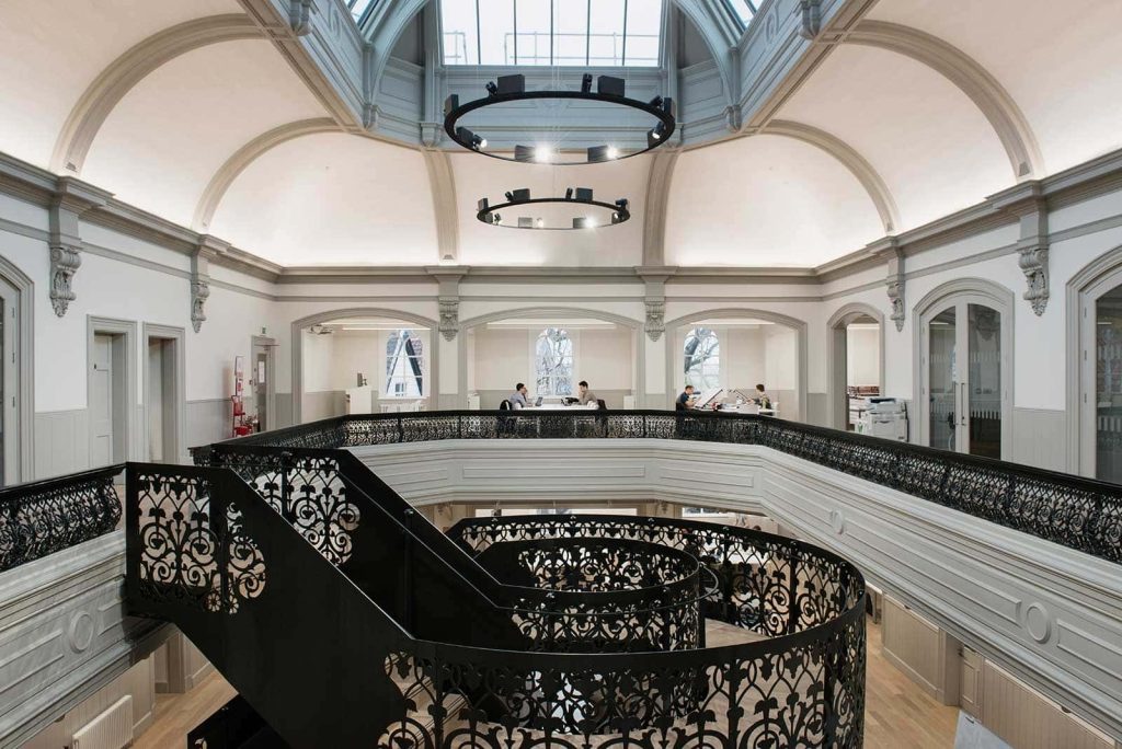 photo of Norwich University of the Arts building boardman house shows large atrium with circular staircase in center with upper level wall with black metal railing and large white curved walls