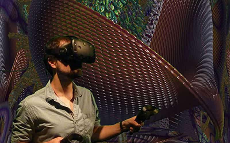 photo of person using virtual reality headset and handheld controllers against backdrop of the mutator exhibit showing scaly abstract 3D objects in organic forms