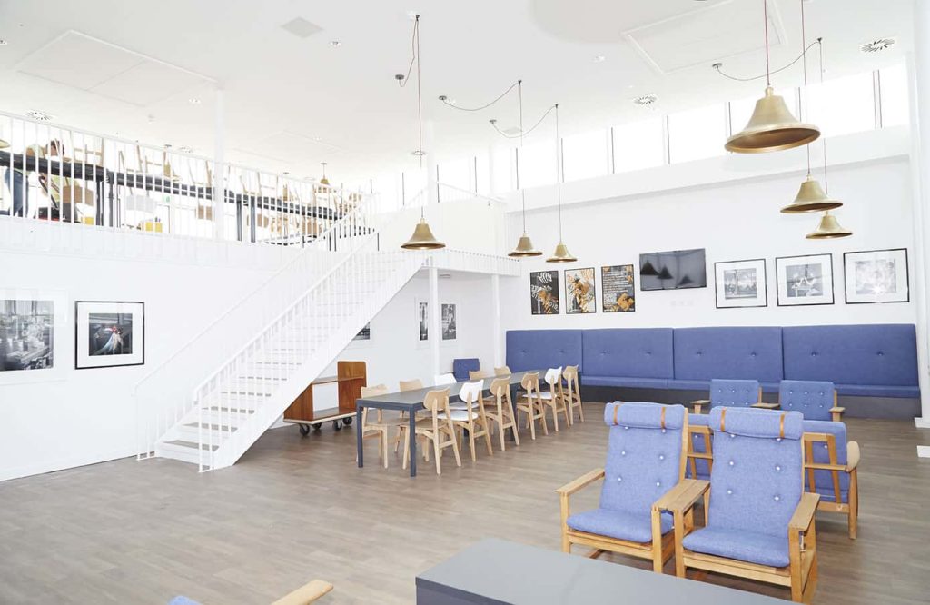 interior photo of Norwich University of the Arts building All Saints Green building shows high ceiling room with white walls and wooden floor with chairs, tables and shelves with books and high windows letting in bright light