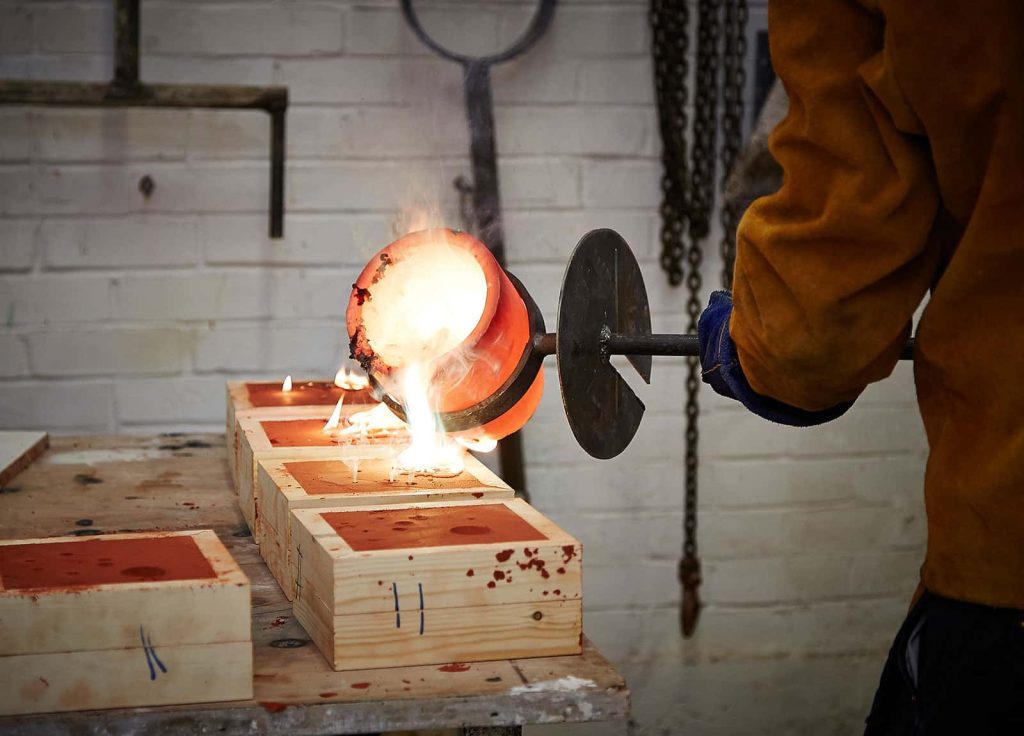 Image of a man pouring hot metal into clay forms