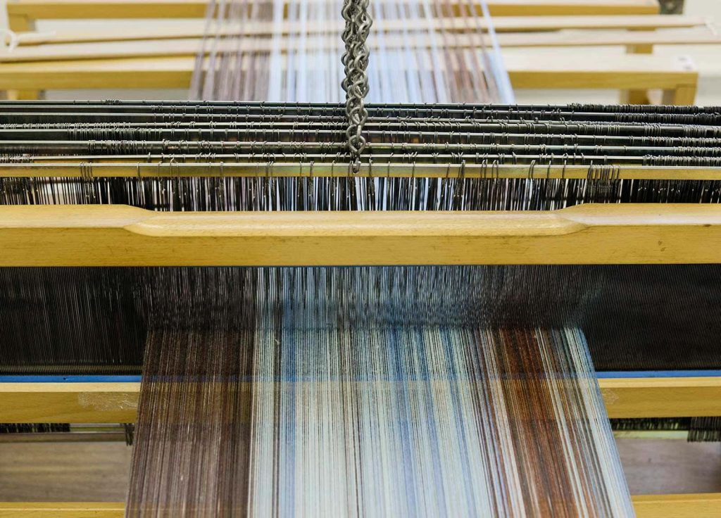 Image of thread on a traditional loom machine. The thread is blue, red and brown in colour