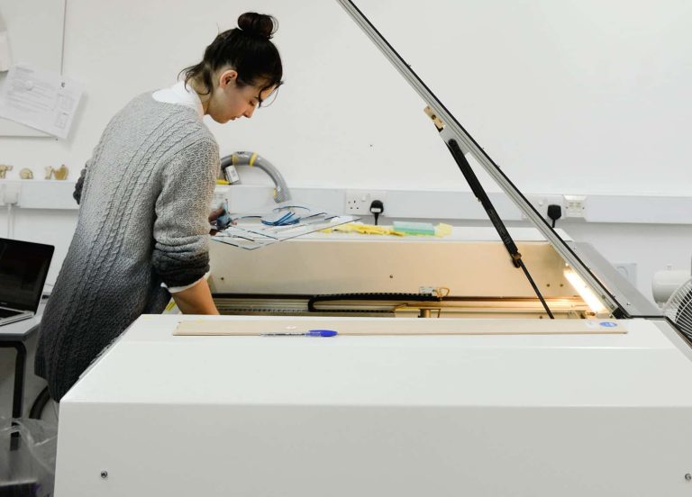 Image of a student working on a laser cutting machine with the lid open above her head