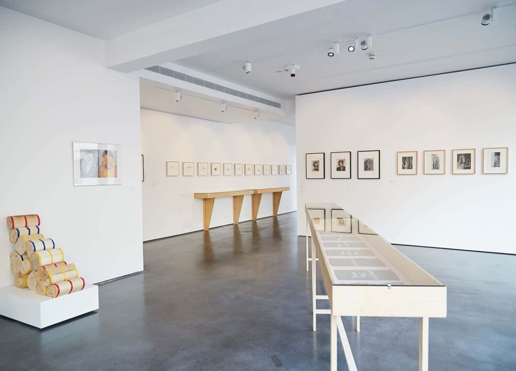 Image of an exhibition featuring work in frames on walls and vitrines of publications