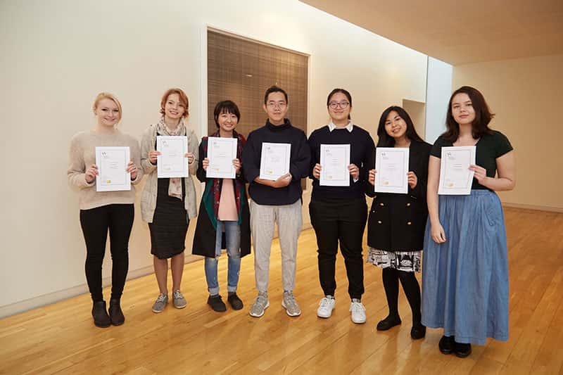 seven students stand in a row holding up A4 certificates