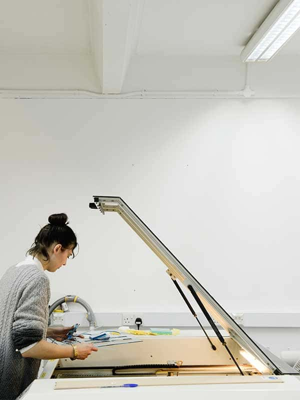 Image of Norwich University of the Arts student leaning under the hood of a laser cutting machine