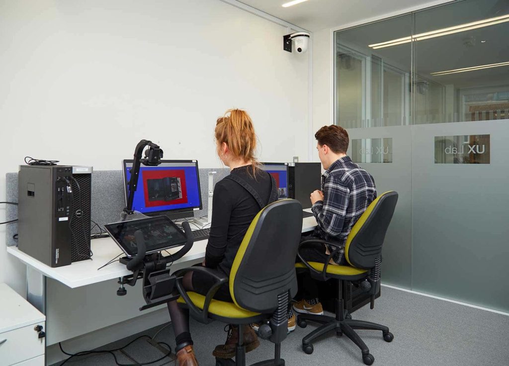 Image of two people working in Norwich University of the Arts's UX Lab. Both people are using a computer whilst being filmed by a tracking camera