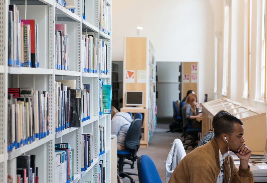 Students working in the Library, between shelves of books and the high windows