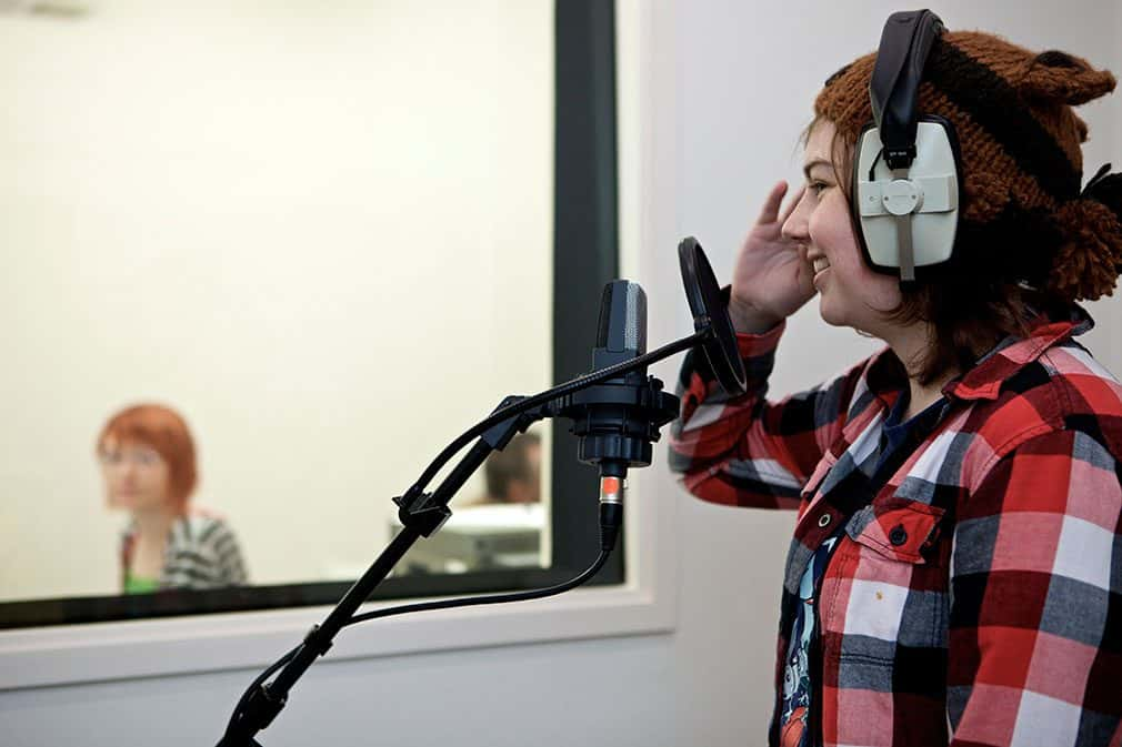 A student wearing overhead headphones and standing in front of a microphone on boom arm with attached diffuser