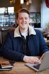 Image of alumni Adam Avery sat in a bar working on his laptop