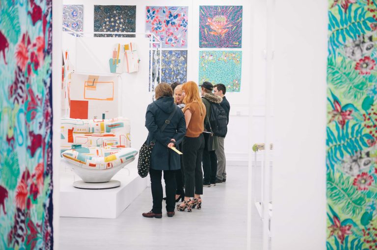 Group of people looking at colourful textiles work in 2016 BA Degree Show