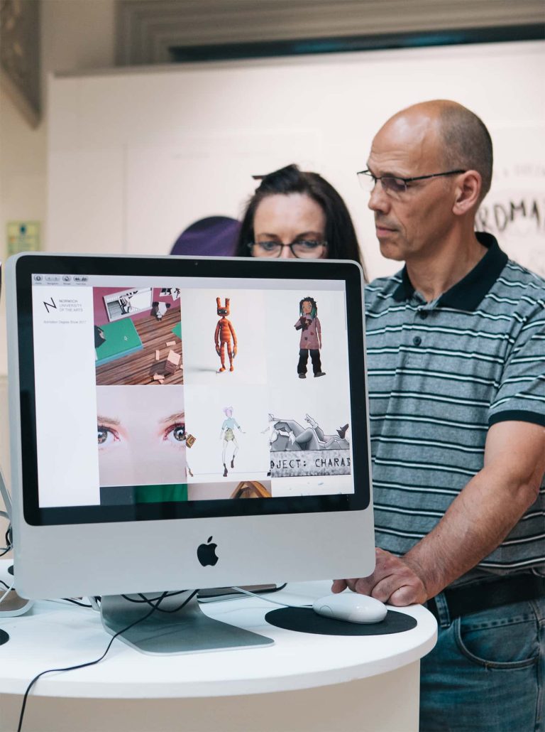 Photograph from BA Degree Show 2017 of two people using a mac to look at digital work