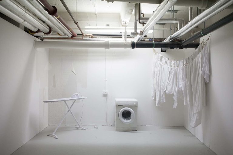 Installation from BA Degree Show 2017 of a white washing machine, ironing board and hanging clothes in a white space