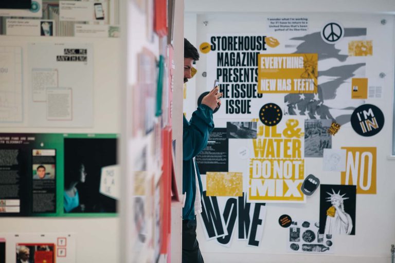 Photograph from BA Degree Show 2017 of someone using their phone amongst colourful graphic design work