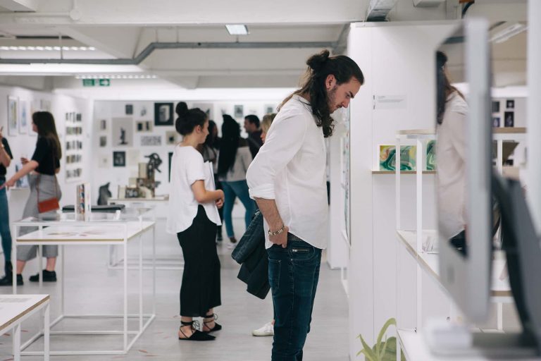 Photograph from BA Degree Show 2017 of people looking at work on tables and stands