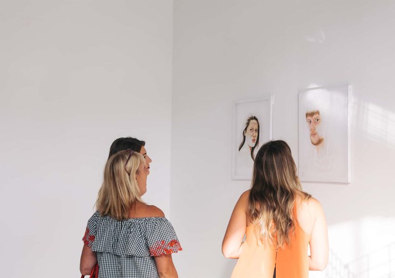 Photograph of three people looking at painted portraits in 2017 BA Degree Show