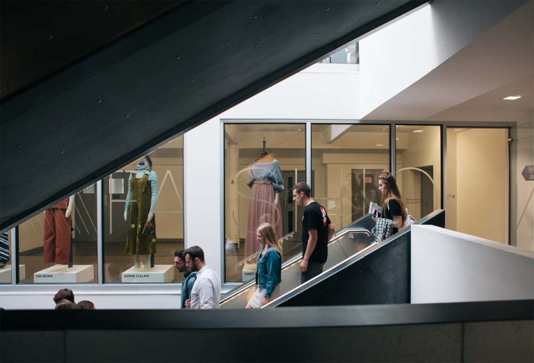 Photograph from Degree Show 2017 Private View of people descending stairs in Guntons in front of fashion mannequins