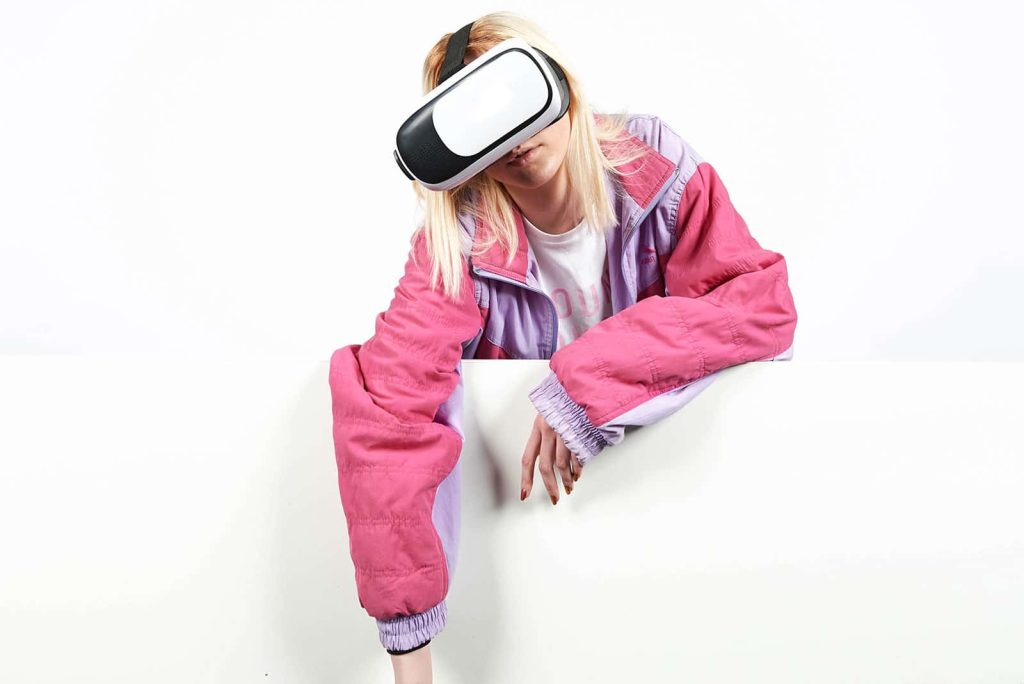 Woman wearing a VR headset with her arm hanging over a white wall