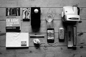 Work by Norwich University of the Arts Research Student John Bournsell showing various objects on a table including matches, shell, phone, glass, ball, camera and book