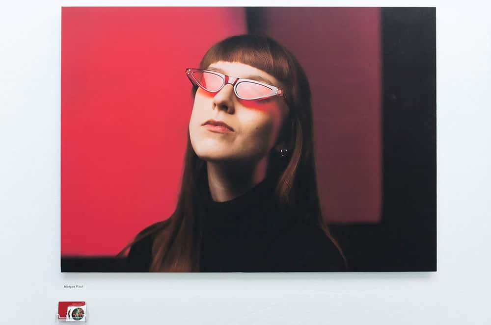 Andy March BA Photography 2018, model with red sunglasses on blurred red background, with straight brown hair and bangs