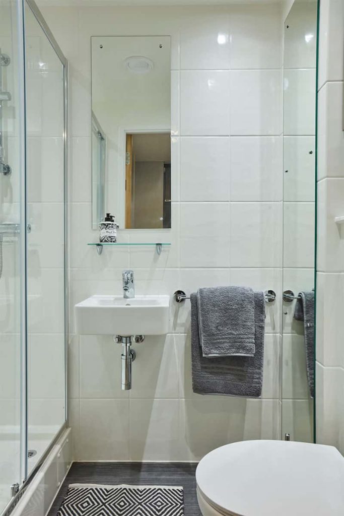 A clean bathroom with white tiled wall, glass shelf, wall mounted china sink