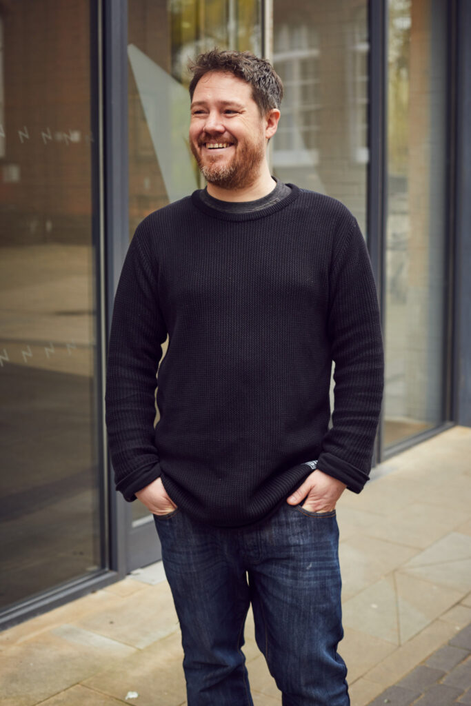 David Watson, Norwich University of the Arts graphics Lecturer standing outside the Guntons building in Norwich in a black jumper