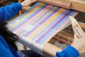 Rebecca Hiscock looking at her loom with coloured weave on