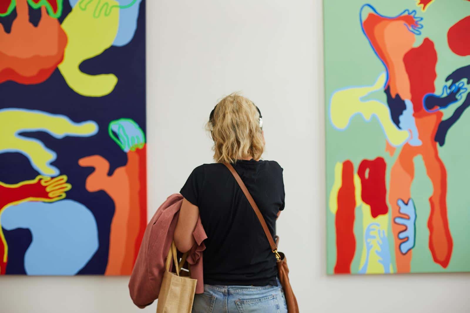 A visitor wears headphones at the Norwich University of the Arts Degree Shows and looks at brightly coloured art