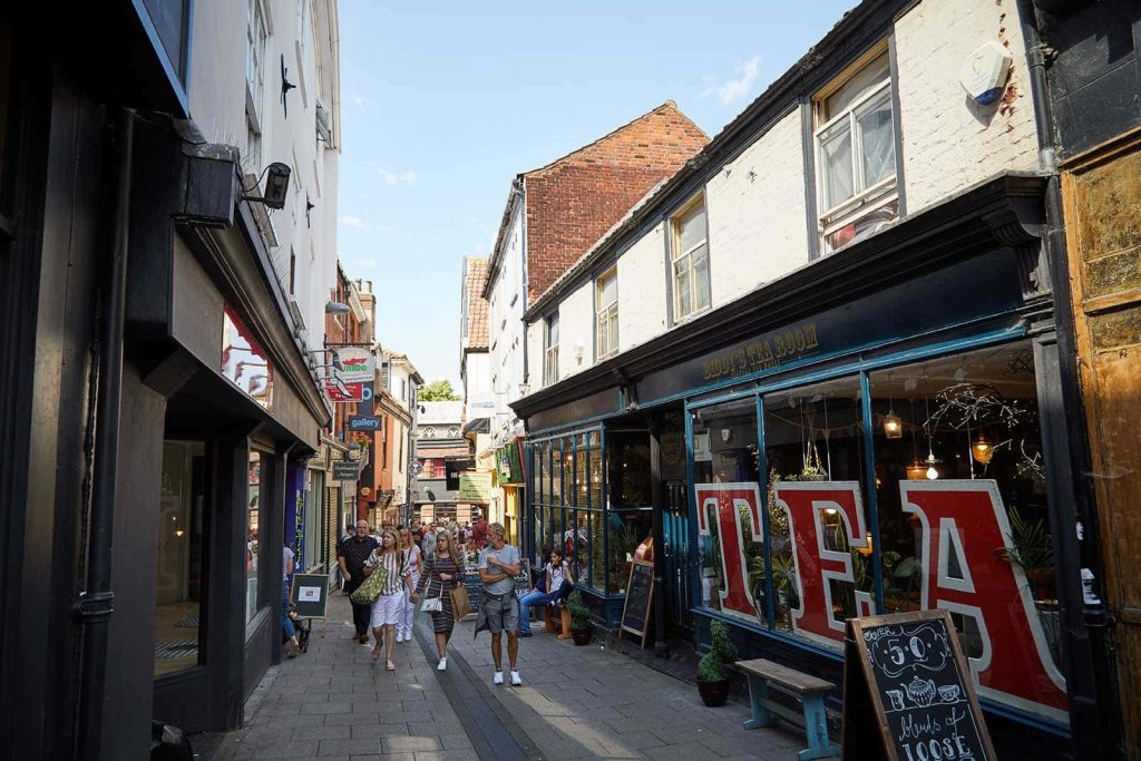 People walking down Lower Goat Lane and Biddys tea room with the words 'tea' in the windows at the Norwich Lanes Fair