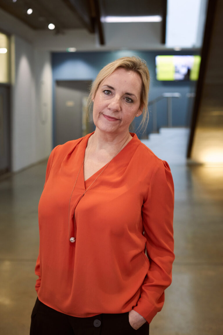 BA Illustration Course Leader Gill Sampson standing in the Norwich University of the Arts Guntons Building wearing bright orange shirt