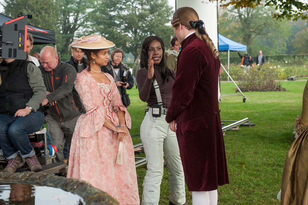 Amma Asante standing on set next to two actors in period outfits