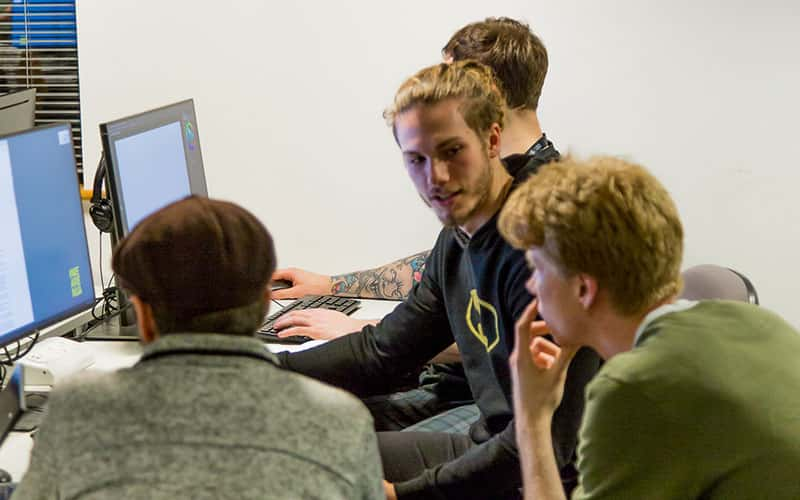 Photo of four men sat talking to each other in front of a computer