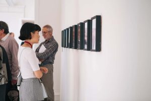 A visitor to the Norwich University of the Arts undergraduate degree show stands looking at multiple frames on a wall.