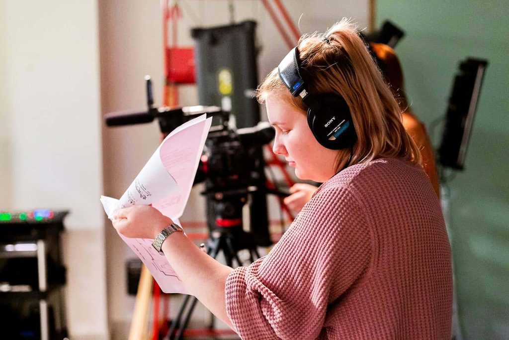 Student working in the Sir John Hurt studio at Norwich University of the Arts holding a call sheet next to a camera with headphones on