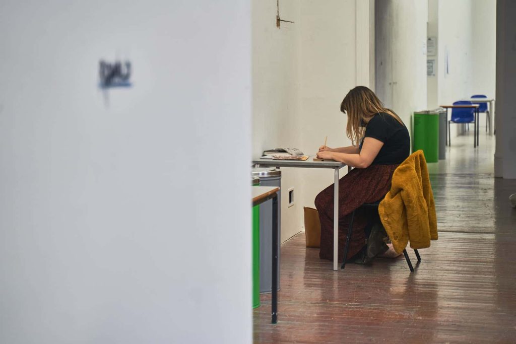 Fine art student working socially distanced. Sitting on chair at desk drawing