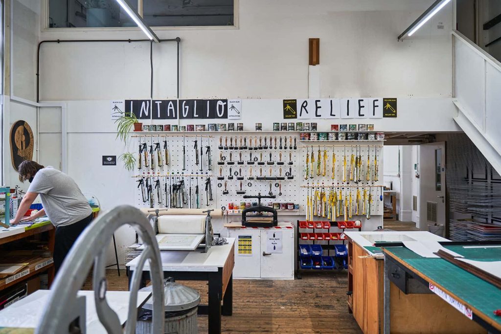 covid safe printmaking studio with person working on artwork. Lots of tools hanging up in background