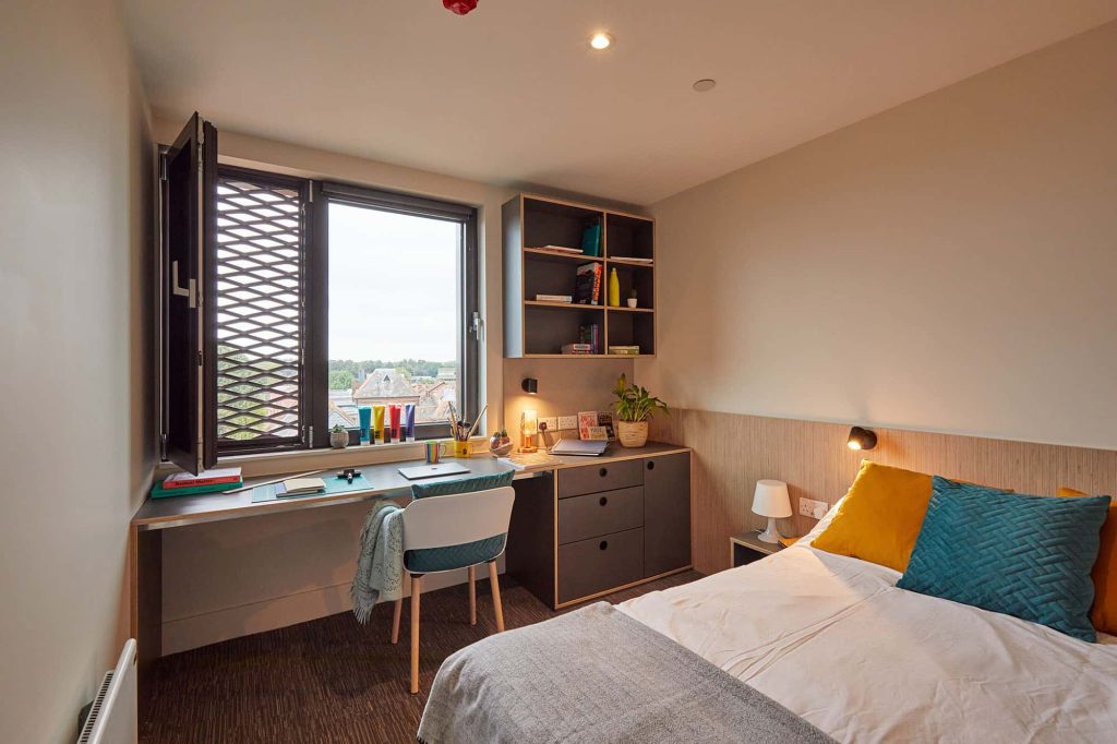 Bedroom at Duke Street Riverside showing a living area; bed, cushions, duvet, throw, green chair by a desk