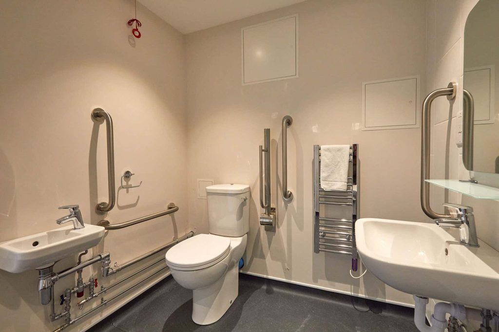 A fully accessible bathroom in Duke St Riverside showing a sink, rails, toilet, towel on radiator and sink with mirror