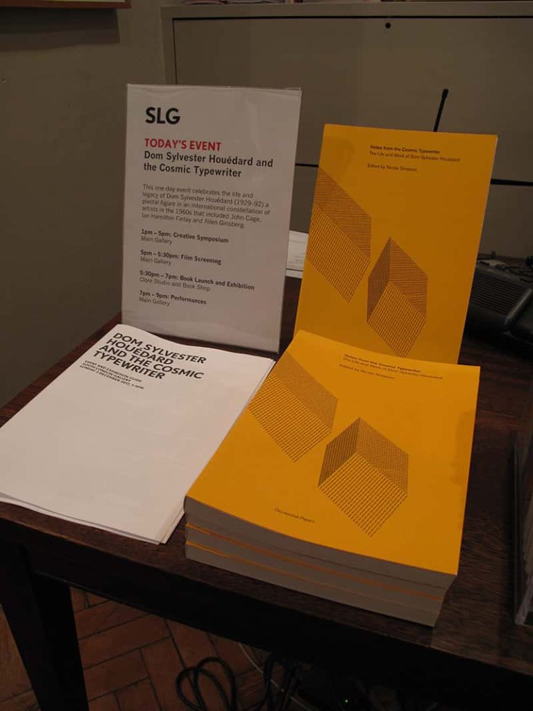 two stacks of pamphlets, one stack is white and says on the front Dom Sylvester Houédard and the cosmic typewriter. The other stack are all yellow and have two cubes printed on the front cover