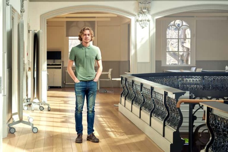 BA Architecture student Bradley Fletcher standing in the architecture studio, next to a black railing balcony