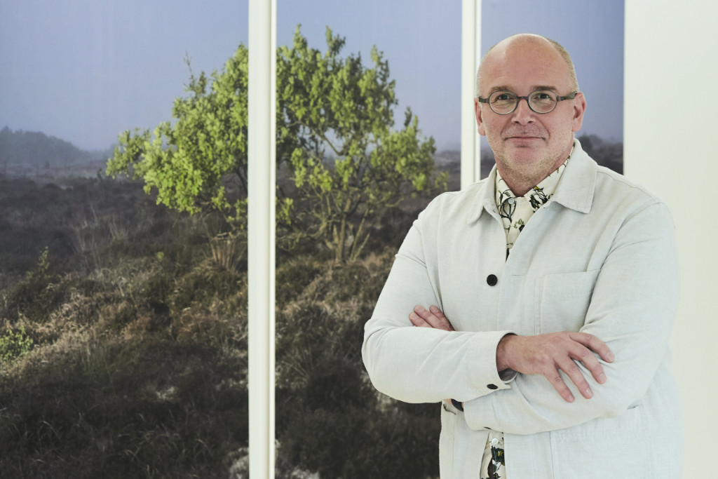 VC Professor Simon Ofield Ker standing in white room with window behind them. They have a white denim jacket on, black trousers and glasses