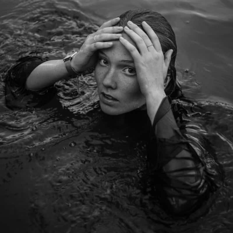 Black and white photo of a young woman submerged in water with her hands on her head